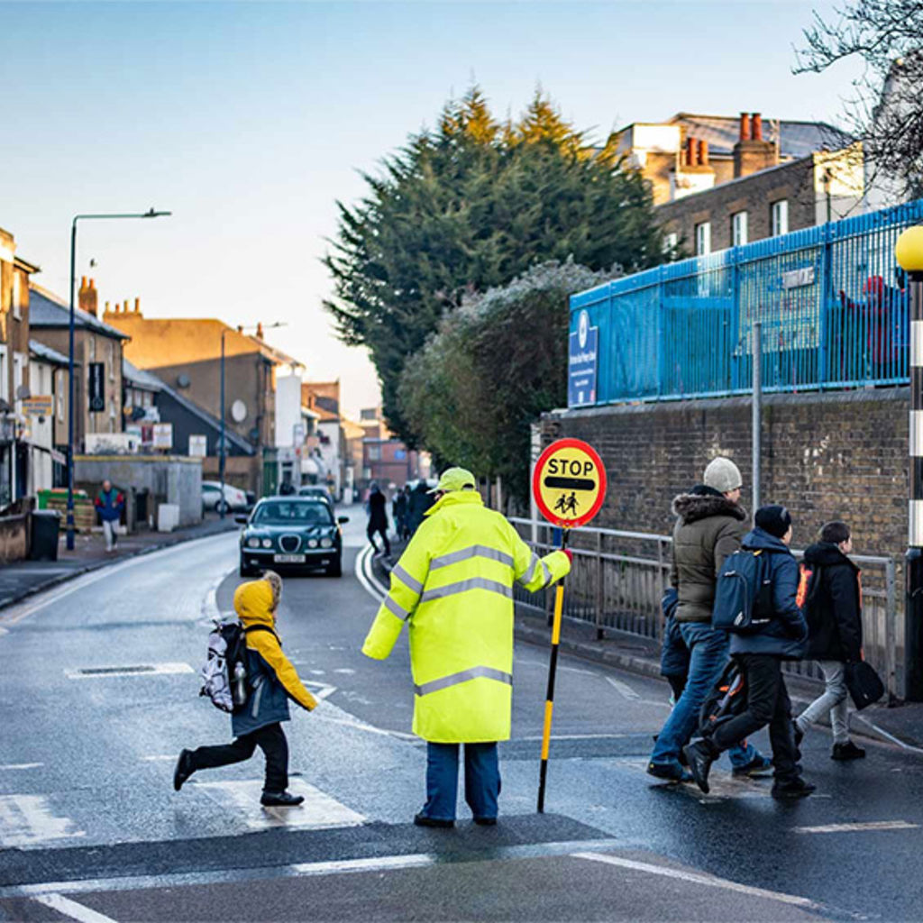 Children cross a road with a lollipop lady